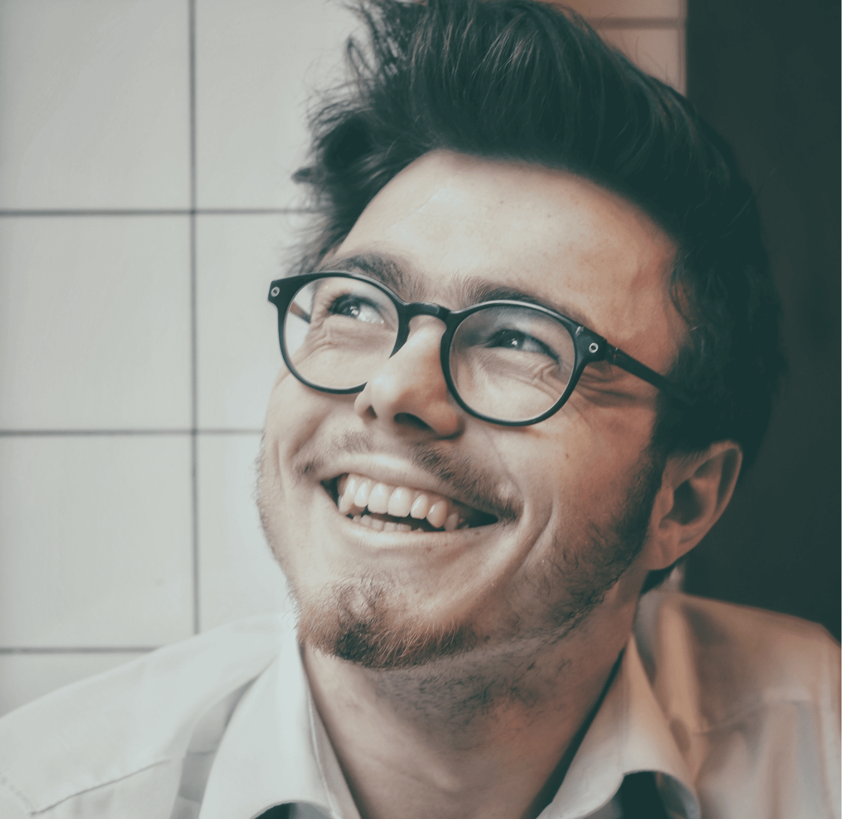 A man smiling to the camera, wearing glasses